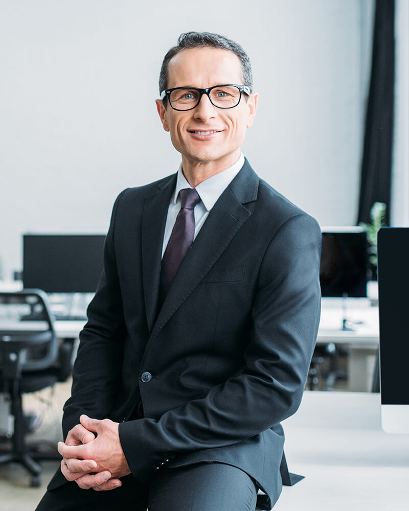 smiling-businessman-in-eyeglasses-sitting-on-table-V5AWVKC.jpg